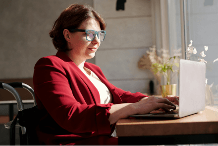 A woman in a smart red jacket sat at a desk using a laptop