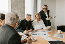 A team of five people are sat around a meeting room table, discussing statistics