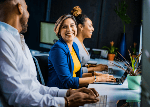 A lady wearing blue and yellow smiles while working with her office colleagues