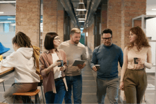 A team of 4 walking through an office building, holding drinks and discussing topics