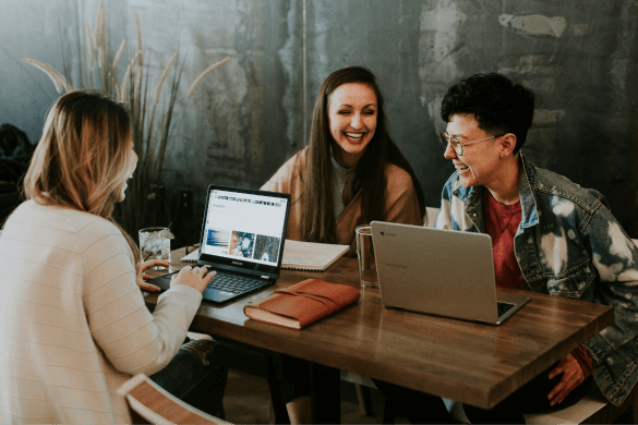 Three young people sat at a table laughing and using laptops