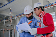 Two people wearing hard hats and safety gear, review documentation on construction site