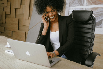 A businesswoman smiles while on the phone and using a laptop